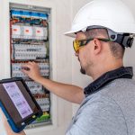 Man, an electrical technician working in a switchboard with fuses. Installation and connection of electrical equipment. Professional uses a tablet.